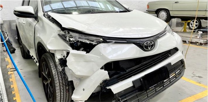 A white Toyota RAV4 in the CHICHO Panel Beating workshop with the front bumper, wing and headlight torn off in a collision.